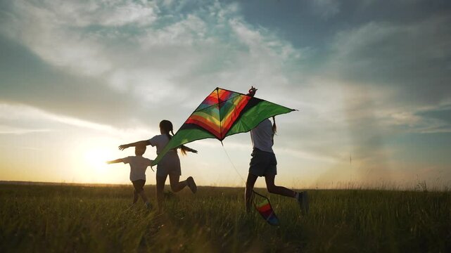 Children play outside with kite at sunset. Children running joyfully fly colorful kite. Happy childhood memories. Siblings in park having fun. Children kite play excitement. Summer outdoor activities.