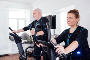 Couple of elderly people in ems suits are engaged in sports equipment.