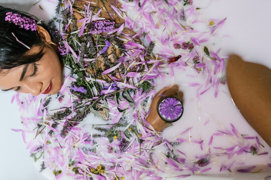 Young woman relaxing in a floral bath with candles