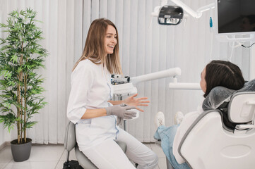 Happy woman dentist and patient teenage girl talking about dental treatment sitting on a dental...