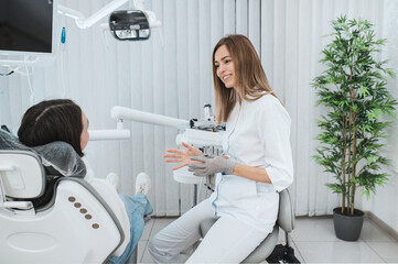 Happy woman dentist and patient teenage girl talking about dental treatment sitting on a dental...