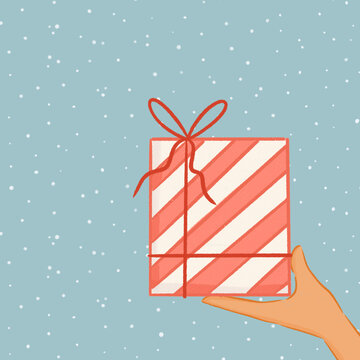 Hand holding a wrapped gift in a snowy Christmas scene