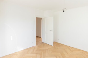Empty room with wooden floor and white walls in a home under construction.