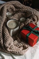A white ceramic mug with cappuccino, candles, red and green gift boxes are on the table. Winter composition. Christmas Card