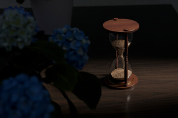 Wooden sandclock on a table with flowers in a dark room