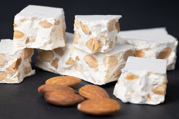 Pieces of hard nougat, with almonds next to it, on a dark slate surface.
