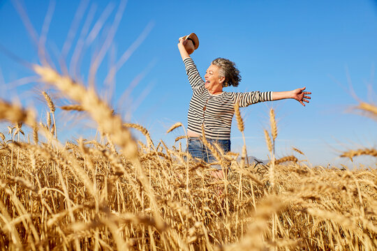 Cheerful mature woman with hat walking in wheat field