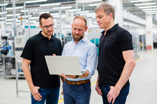 Businessman sharing laptop with employees in a factory