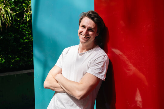 Smiling man with arms crossed leaning on multi colored wall