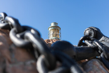 Naklejka premium Primer plano de una cadena de ancla con una lámpara marinera al fondo bajo un cielo azul claro, creando una atmósfera marítima y serena. Vilanova i la Geltrú