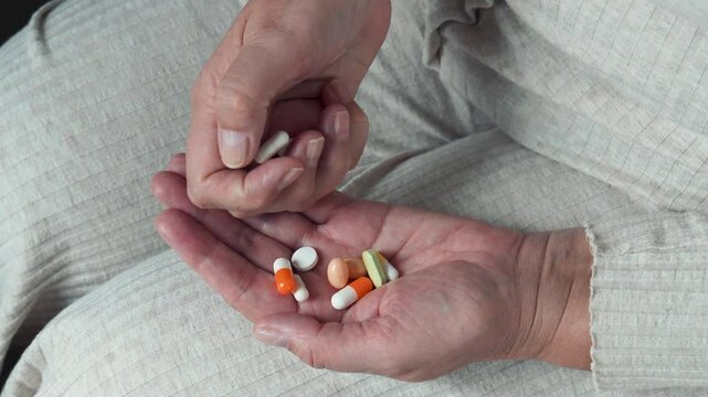 Elderly woman counts pills in her hand while wearing beige pajama. Scene highlights importance of medication management in daily life and emphasizes health and wellness. Taking pills for sick people