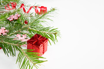 Closeup of pine branch, snow flakes, red colored Christmas decoration box on white background with copy space