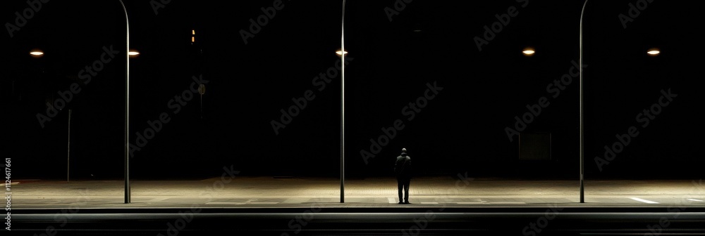 Poster a solitary person stands on an empty street at night, illuminated by soft streetlights that create l