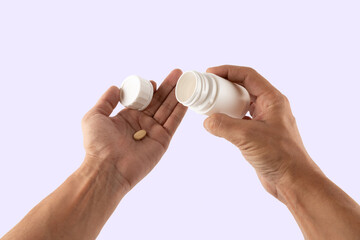 Male hands holding a pill from a white medicine bottle isolated on light purple background