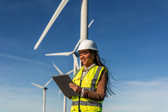 Latin american female engineer using tablet in wind turbine power plant generating green energy