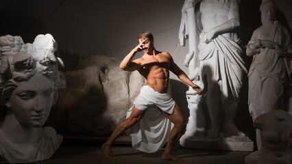 A muscular man in a tunic, antique aesthetics, a bodybuilder among sculptures.