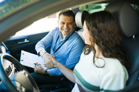 Happy driving instructor shaking hands with his student after passing the driving test inside a car - Powered by Adobe