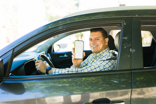 Hispanic driver showing blank screen smartphone app while driving a car, ride sharing and carpooling concept