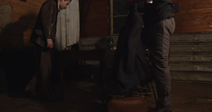 Three men sit down at a table in a dark and shady hideout