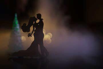 Black silhouettes of pair dancers performing. Man and woman are dancing on gray background with white backlight. Choreography. New Year's ball