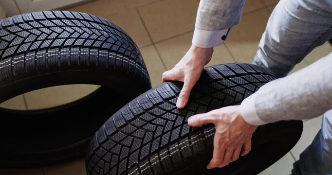 Guy carefully checks strength of tire treads with hands. Man evaluates durability to make sure work surface in context of reliability