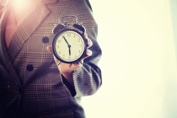 A young woman in a stylish suit holds an alarm clock in her hands. The concept of the end of the...