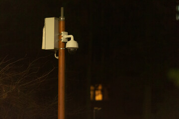 A tall pole with a camera securely attached to it, standing in a dimly lit area during the night,...