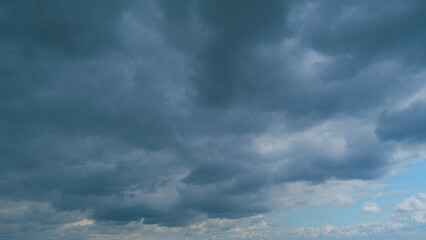 Fototapeta premium Background of dark dramatic sky with stormy clouds. Moving white puffy clouds on blue sky. Time lapse.