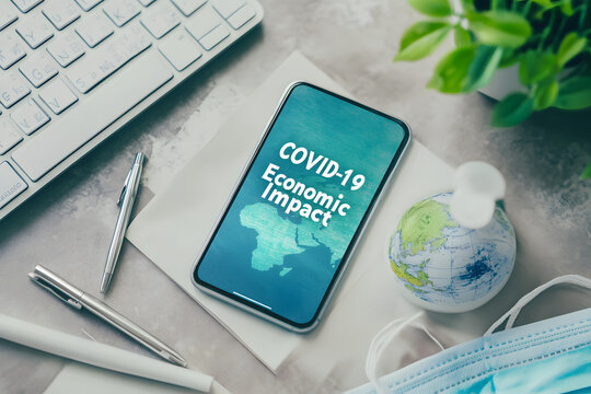 Smartphone showing COVID-19 economic impact with globe, mask, and keyboard on desk, highlighting global financial and health challenges during the pandemic