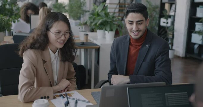 Man and woman colleagues talking looking at laptop screen sharing ideas on business development at desk in office. Company and employee concept.