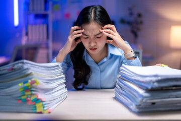A woman is sitting at a desk with a pile of papers in front of her