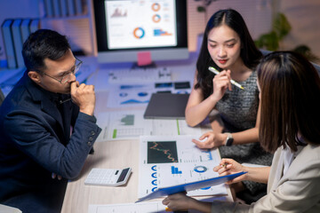 Three people are sitting at a table with papers and graphs in front of them