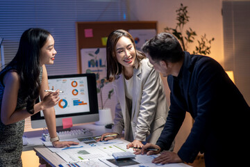 Three people are sitting at a desk with a computer monitor and a whiteboard