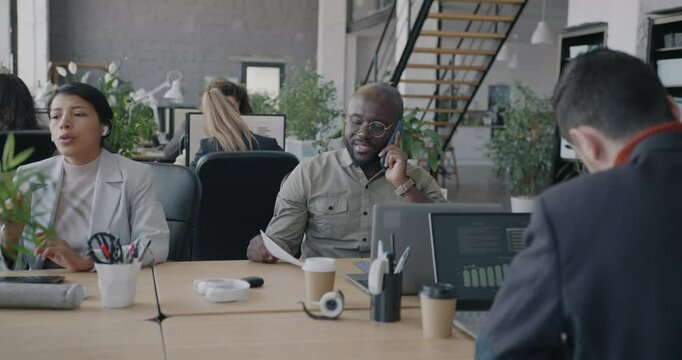 Multiethnic group of businesspeople working in office using computers talking on mobile phone. Workplace routine and diverse staff concept.