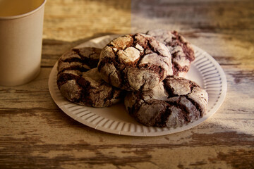 A plate of chocolate biscuits with cracks on an old rustic wooden table in a beam of sunlight