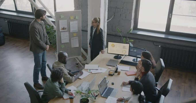 Two businesspeople making presentation to group of specialists speaking pointing at board at meeting in office. Business and teamwork concept.