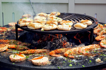 Close-up variety of shrimp and squid grilled over an open flame. Platter of fresh seafood with herbs and spices and sizzling on the grill. Concept of the cooking process street food on fish market