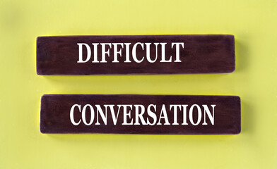 DIFFICULT CONVERSATION - words on brown wooden blocks on a yellow background