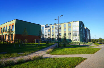 Obraz premium Townhouse along sidewalk with green lawn. Street with sidewalk with flowerbed shrubs and trees. Townhouse in suburb. New apartment buildings in green enviroment. Landscaping for urban spaces.