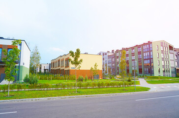 Fototapeta premium Townhouse in a suburb area. New apartment buildings in green enviroment. Street with Two-story townhouses. Modern Townhouse along sidewalk with green lawn. Pedestrian path with flowerbed shrubs.