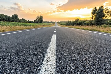 Naklejka premium A serene road stretches into the horizon, flanked by lush greenery under a vibrant sunset sky.