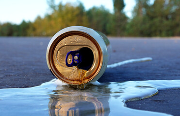 Crumpled beer can on asphalt with spilled alcohol. Discarded broken drink, spilled soda can on...