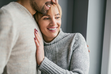A joyful and loving couple sharing a warm embrace while smiling. Both are wearing cozy sweaters, highlighting their happiness and affection.