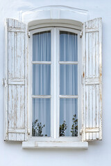 An open window with wooden shutters on an aged white concrete wall.