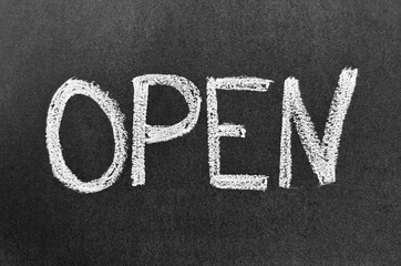 The word "OPEN" is written in white chalk on a dark gray chalkboard. Concept of business announcement.