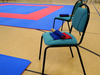 A chair with blue-red flags in front of a tatami in a sports hall, symbolizing the preparation for an exciting martial arts event. © Frank