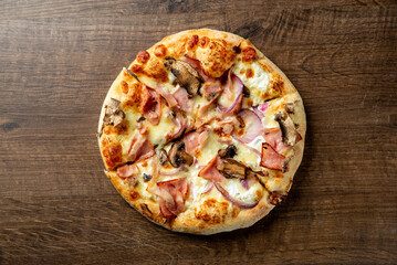 A delicious round pizza topped with ham, cheese, mushrooms, and red onions, presented on a rustic wooden table. Ideal for food-related projects or menus.