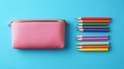 Back-to-school minimalist setup. Overhead shot of a pink pencil case, colored pencils, and a blank notebook on a blue background