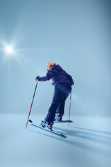 Athletic woman skier in purple jacket leans into precise carve, their skis cutting smoothly against gradient blue studio background. Concept of extreme sport, Christmas holidays. Ad