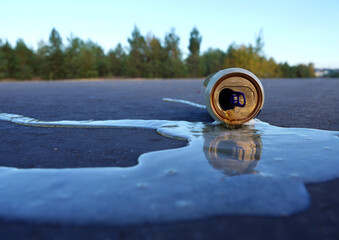 Crumpled beer can on asphalt with spilled alcohol. Discarded broken drink, spilled soda can on...
